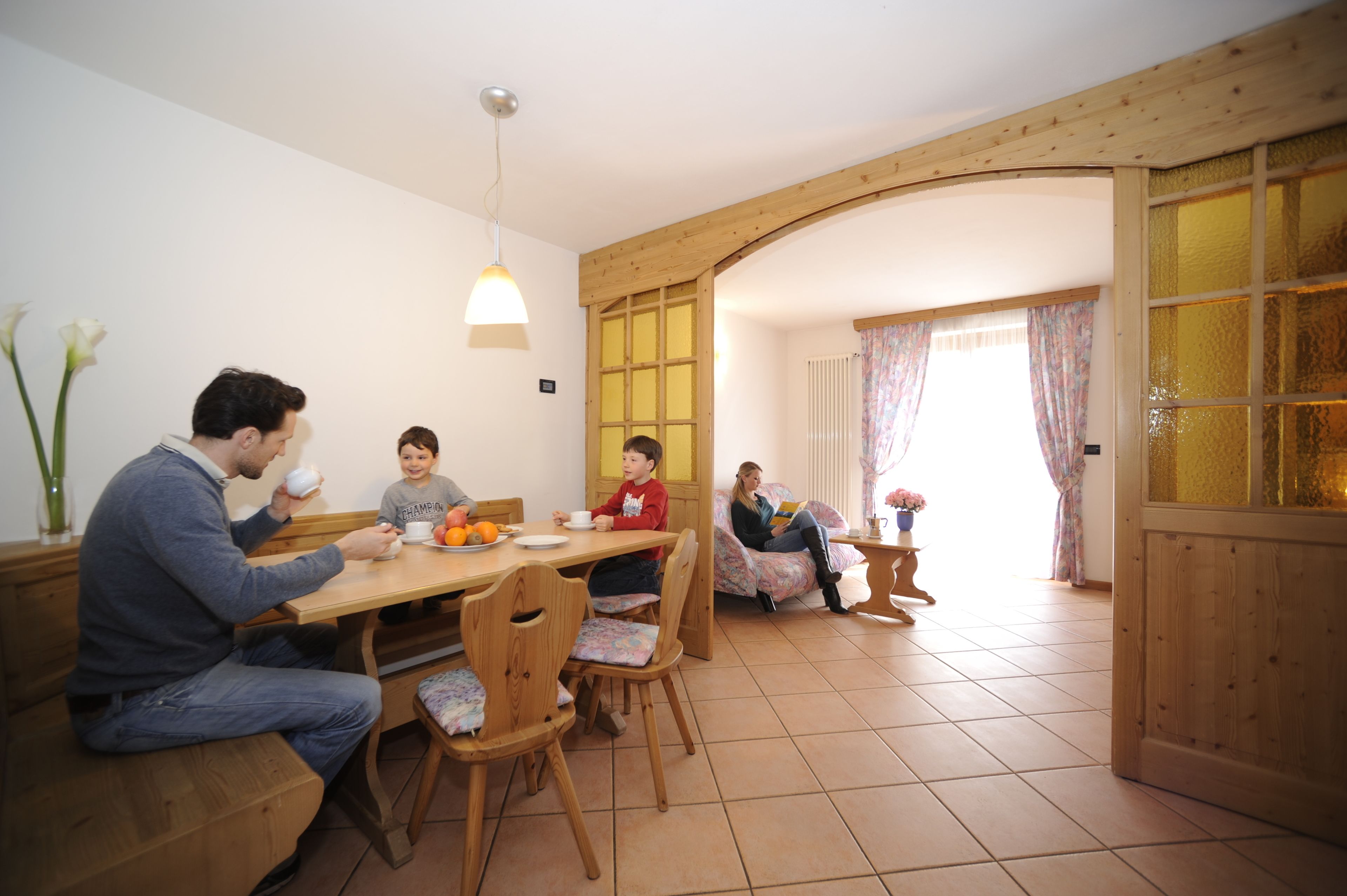 Ein Essbereich mit Holzmöbeln, einer Chandelüster und Blick in den angrenzenden Raum durch eine geöffnete Tür.