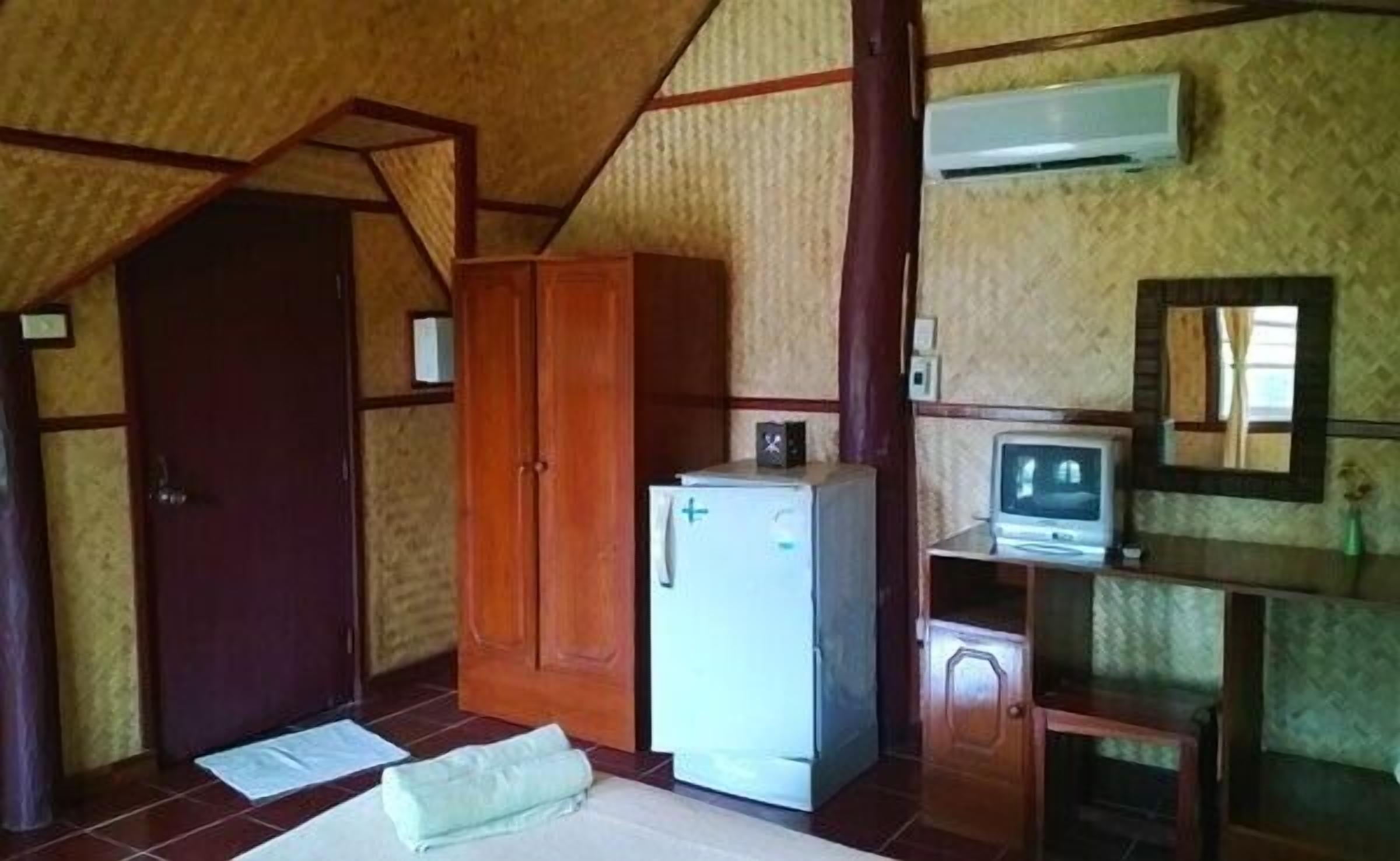 Una habitación con un armario de madera, un refrigerador blanco, un televisor sobre un mueble de madera y un espejo en la pared.