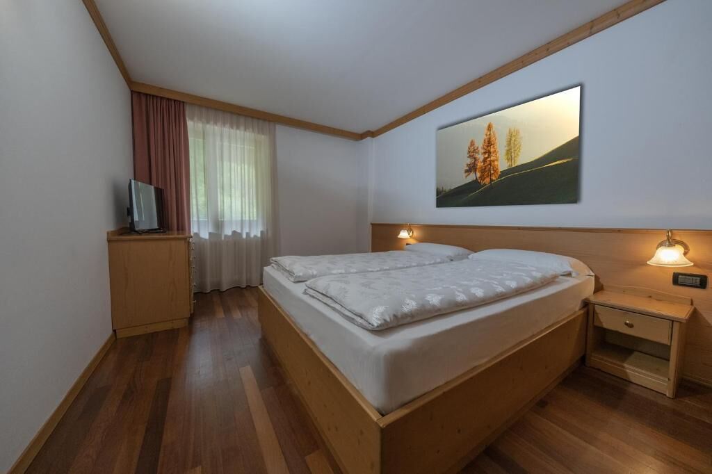 A bedroom with a bed, a nightstand, a television, and a painting on the wall.