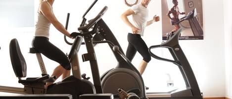 A gym with stationary bikes and treadmills, a clock on the wall, and a poster of a person running.