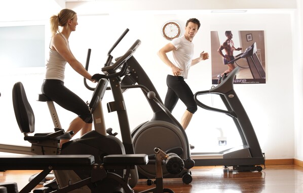 A gym with stationary bikes and treadmills, a clock on the wall, and a poster of a person running. - Residence Kristall (Predazzo)