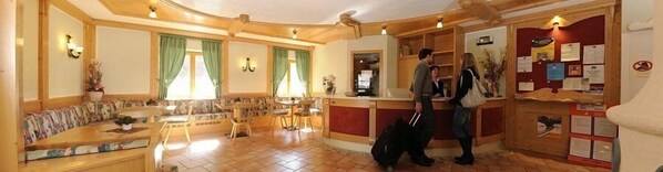 A cozy hotel lobby with a long sofa, a wooden reception desk, and a bulletin board with notices.