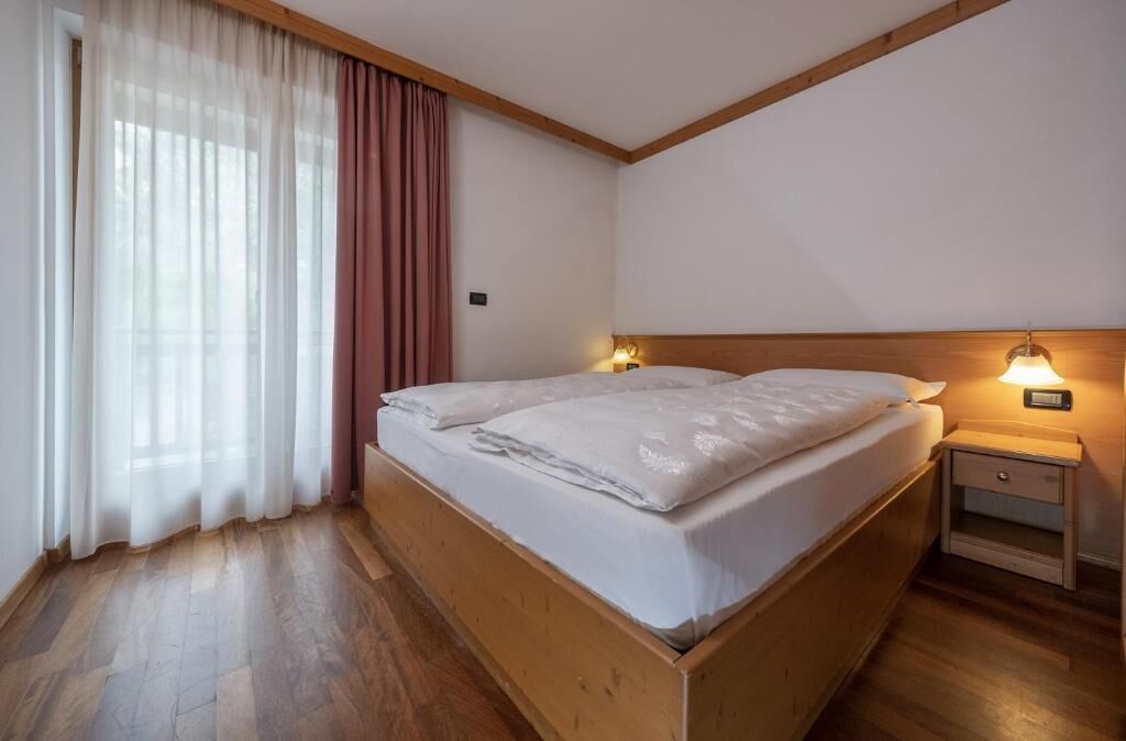 Una habitación con una cama de madera, una mesita de noche con una lámpara y una ventana con cortinas.