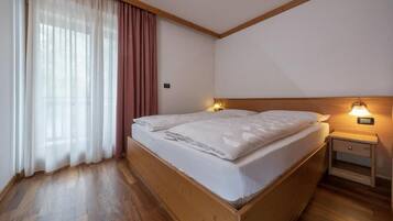 Una habitación con una cama de madera, una mesita de noche con una lámpara y una ventana con cortinas.