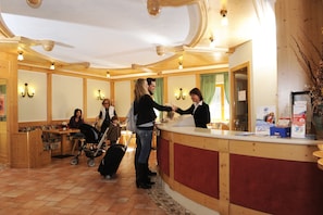 A reception area with a wooden reception desk, a counter, and a seating area with tables and chairs. - Residence Kristall (Predazzo)