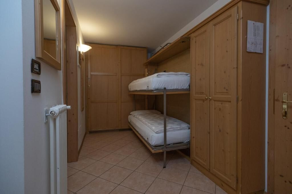 A small room with a bunk bed, wooden wardrobe, and a radiator.
