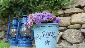 A blue lantern with the word "AMARANDA" and a flower design, placed on a wooden surface with a stone wall in the background. - Amaranda Ada Evi - Adults Only (Bozcaada)