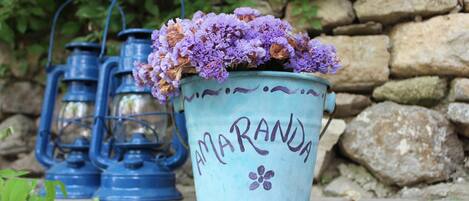 A blue lantern with the word "AMARANDA" and a flower design, placed on a wooden surface with a stone wall in the background.