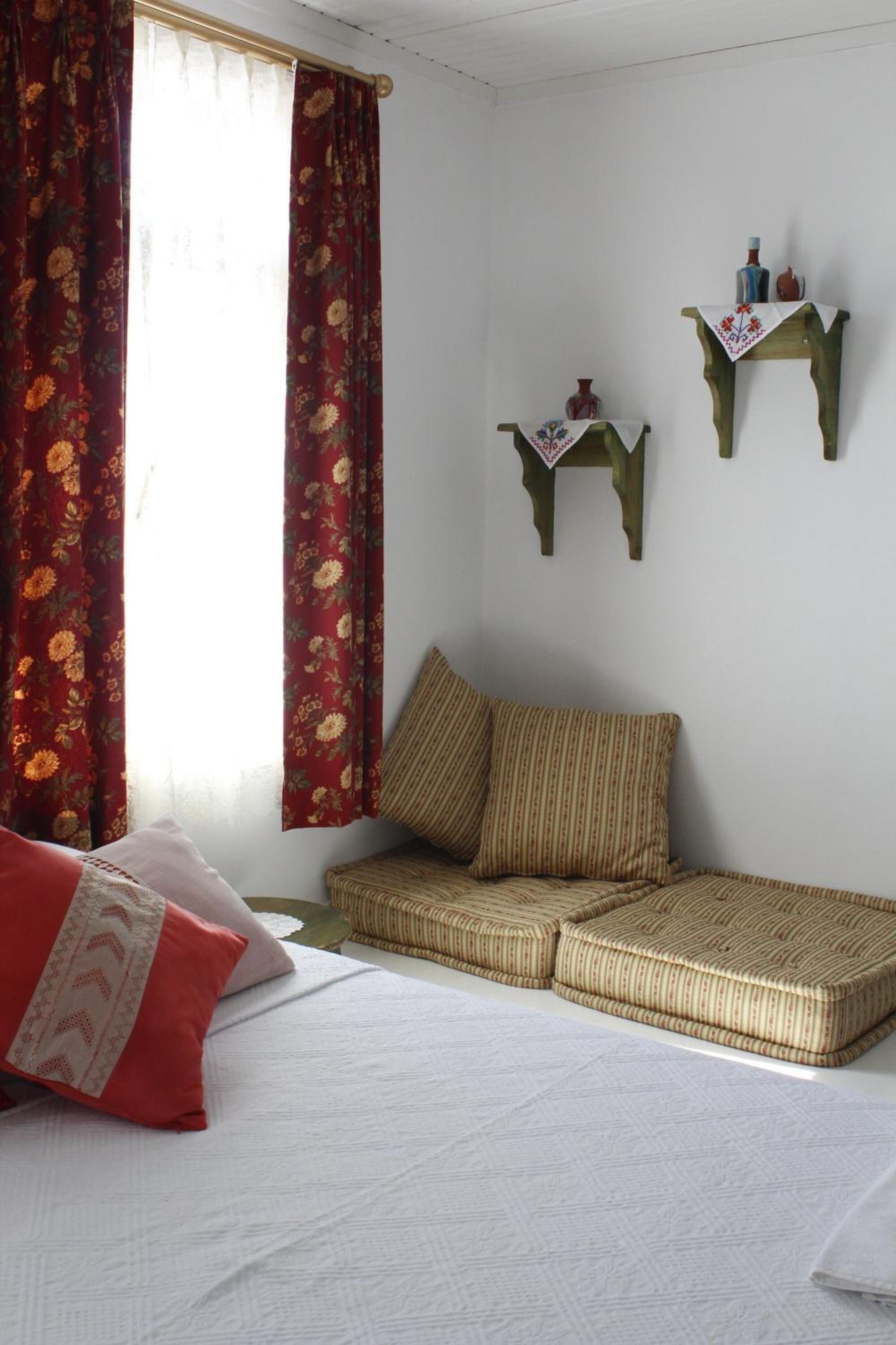 A room with a bed, a woven sofa, a small table with decorative items, and a window with floral curtains.