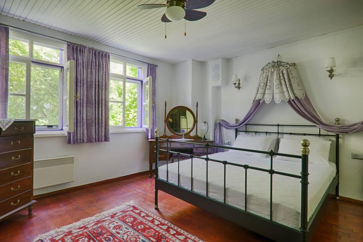 A bedroom with a four-poster bed, a dresser, a mirror, and a window with curtains.
