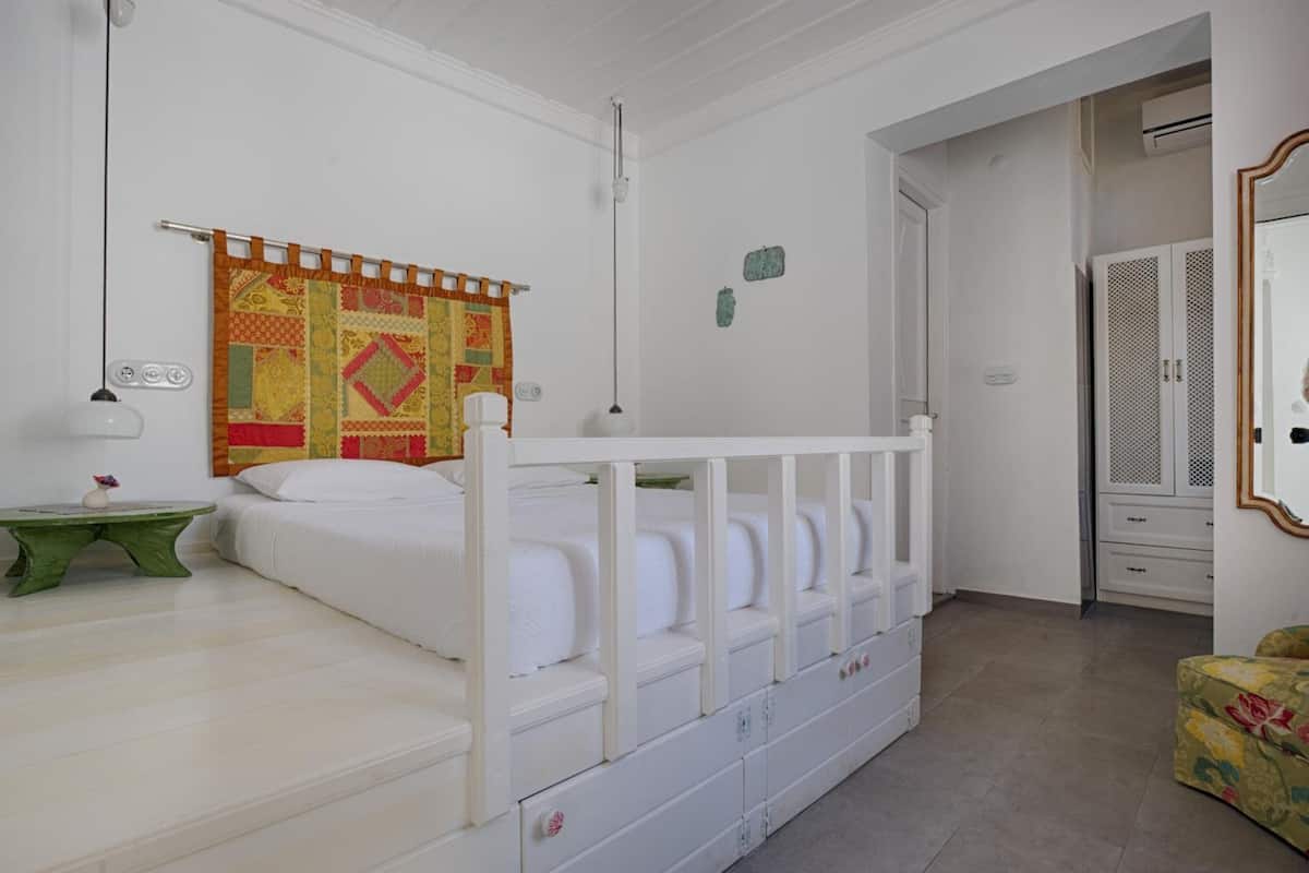A bedroom with a white bed, a green side table, a colorful quilt, and a wardrobe.