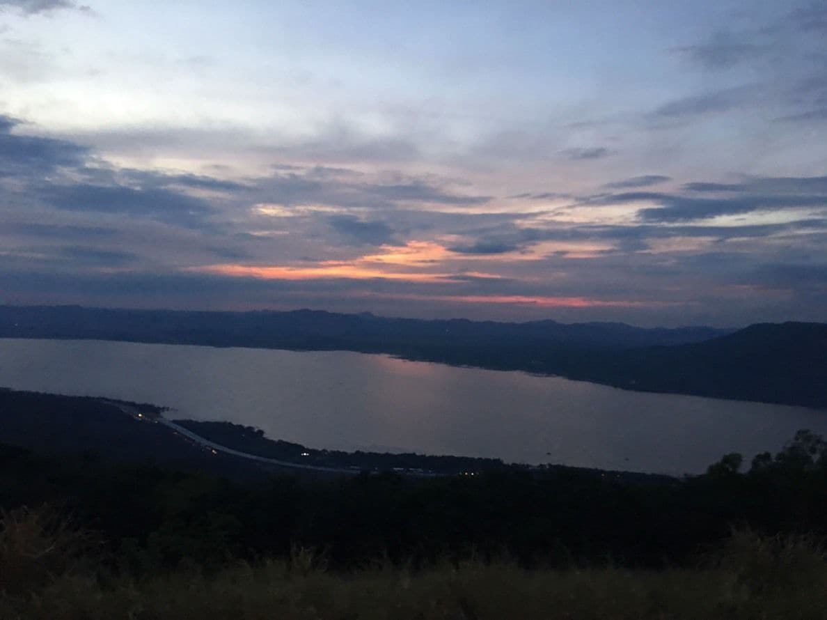 Une vue panoramique d’un lac au crépuscule, avec des montagnes lointaines et une route qui longe le bord de l’eau.