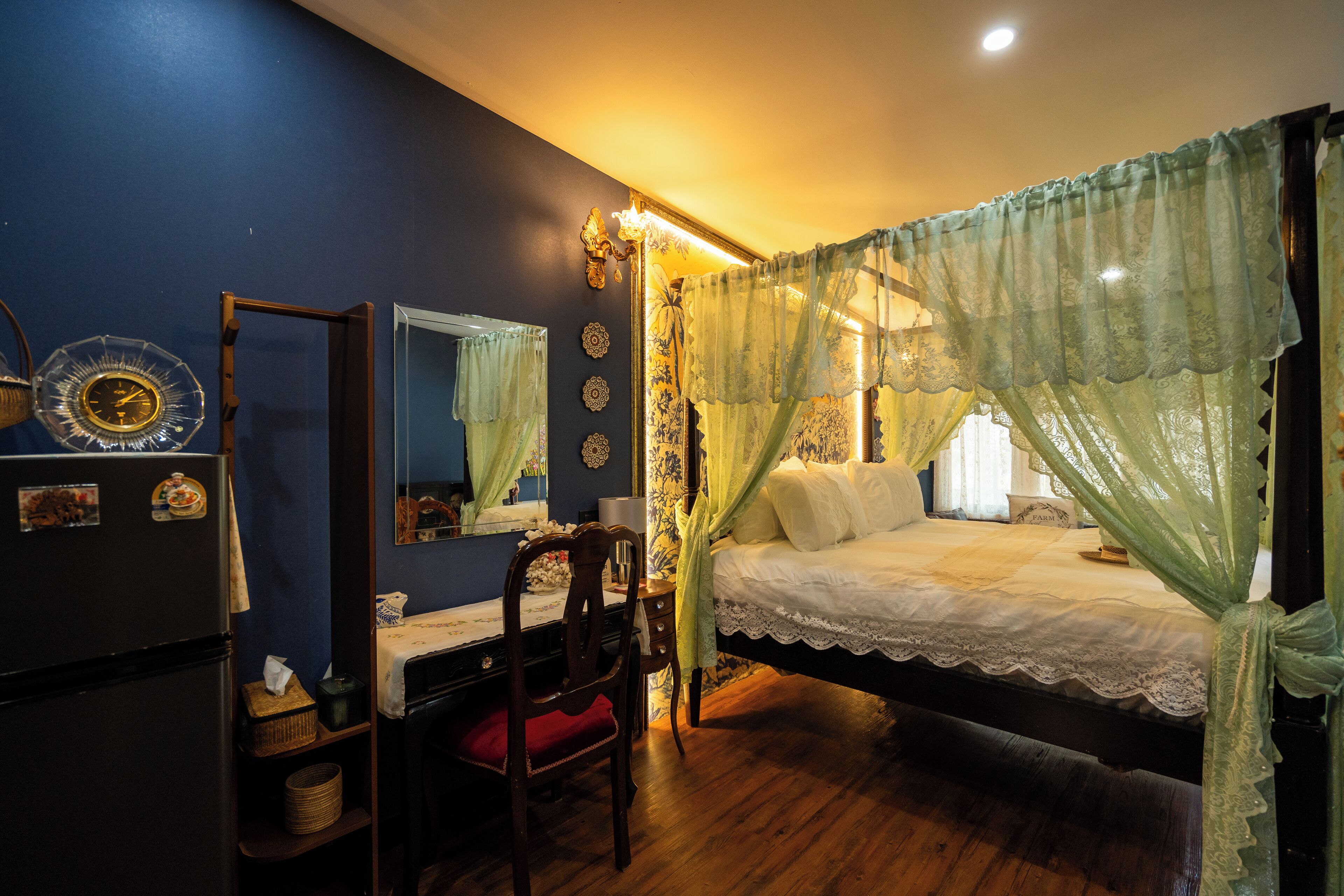 A bedroom with a bed, a desk, a chair, a mirror, and a wardrobe.