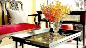 A room with a red sofa, a wooden chair, a small table with a vase of flowers, and a wall decorated with plates. - The Unforgotten B&B (Bangkok)