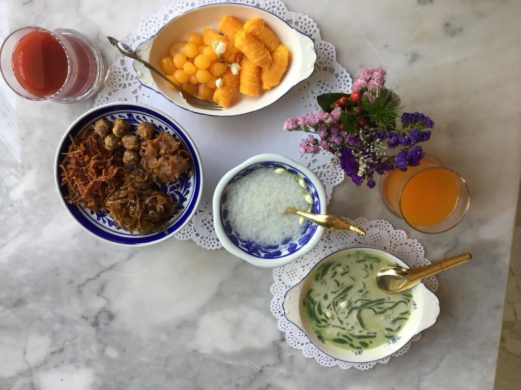 A table with various dishes, including a bowl of orange slices, a bowl of meatballs, a bowl of rice, and a bowl of soup. There are also two glasses of a red drink and a glass of a yellow drink.