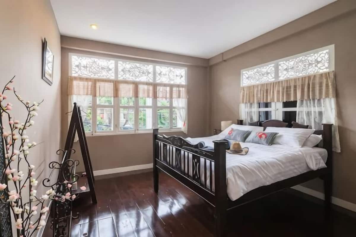 A bedroom with a bed, large windows, and a decorative plant.