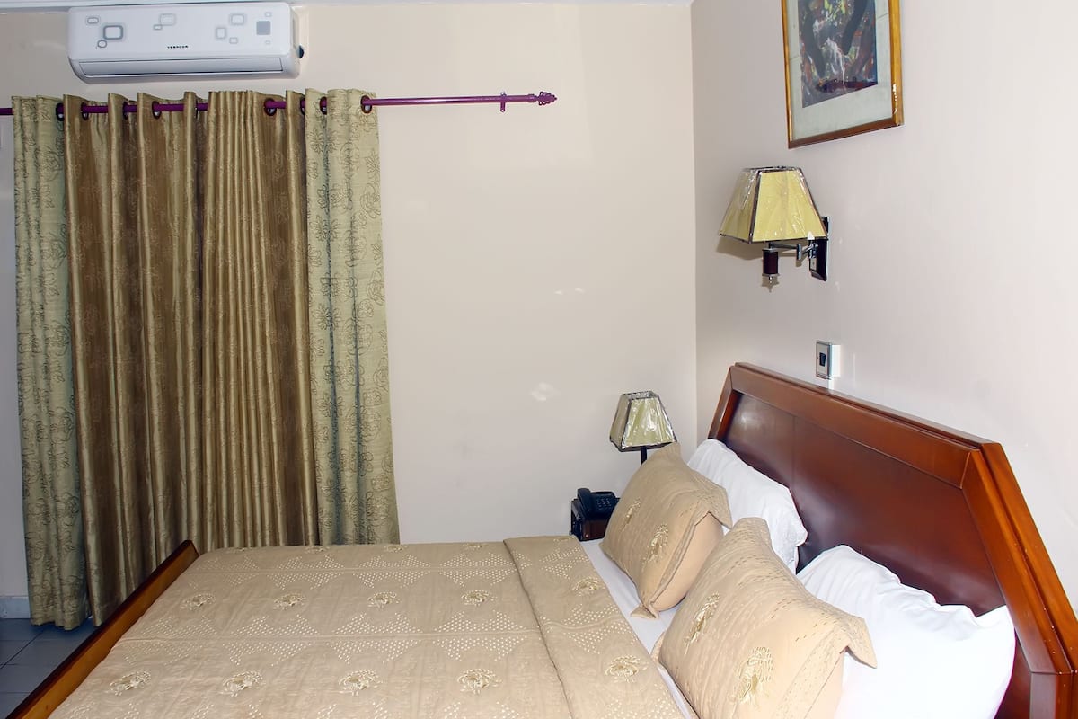 Ein Hotelzimmer mit Bett, Vorhängen, einer Lampe und einem Thermostat.