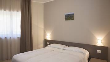 Een net opgemaakt bed met witte beddengoed, twee nachtkastjes met wandlampen, en een klein landschap op de muur.