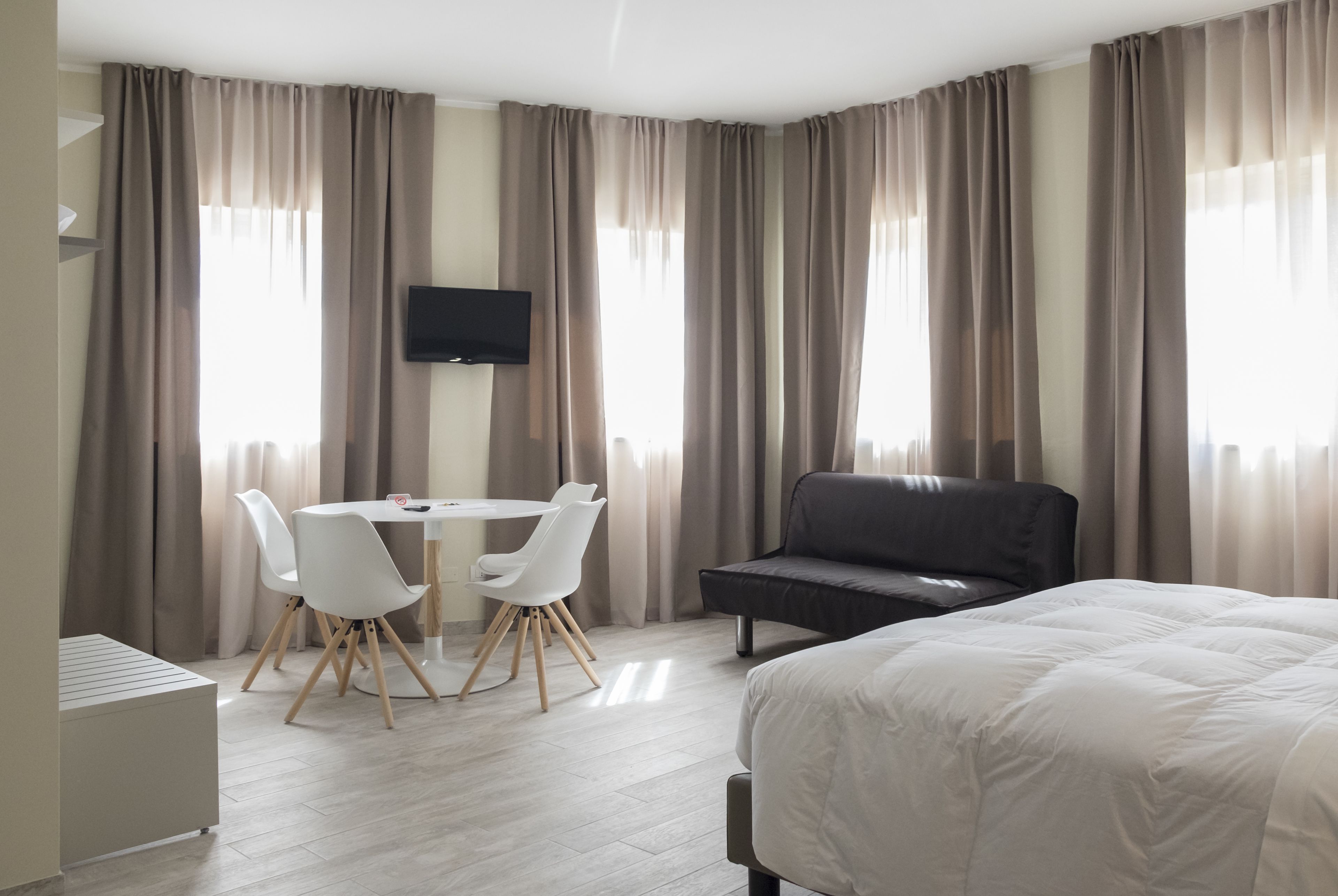Een hotelkamer met een bed, een bureau met stoelen, een televisie en grote ramen met gordijnen.