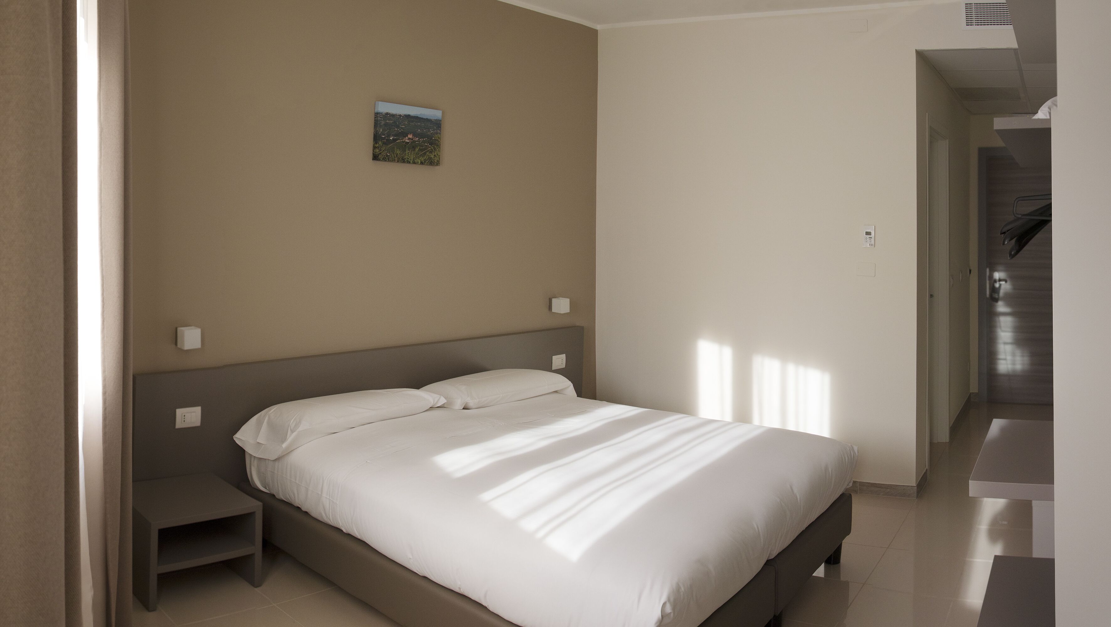 A bedroom with a bed, nightstands, a small picture on the wall, and a door leading to another room.