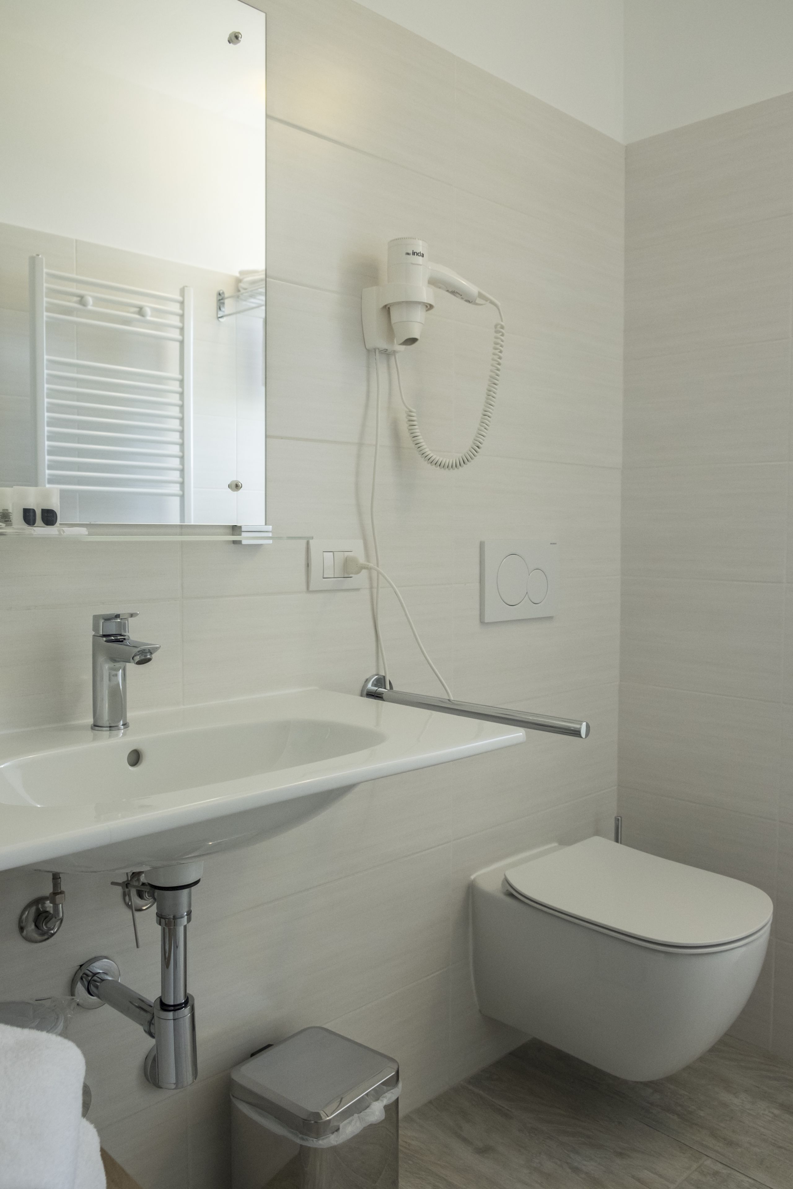 Un baño moderno con un lavamanos blanco, un inodoro y un secador de pelo montado en la pared.