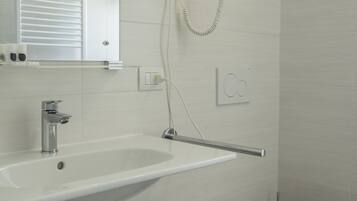 Un baño moderno con un lavamanos blanco, un inodoro y un secador de pelo montado en la pared.