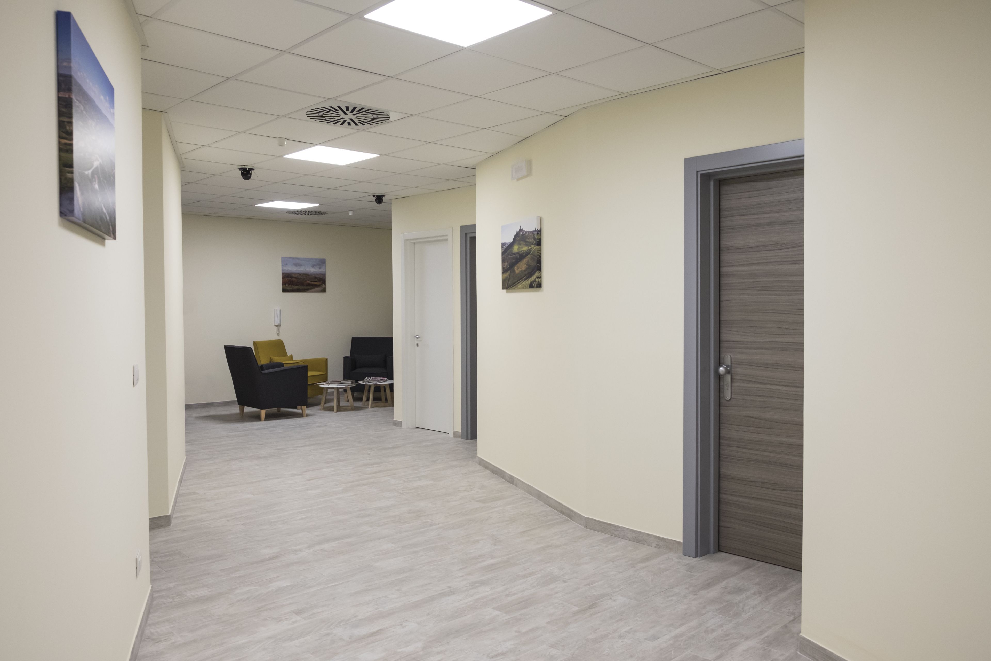 A hallway with a light-colored floor, a closed door on the right, and a chair with a yellow cushion in the distance.