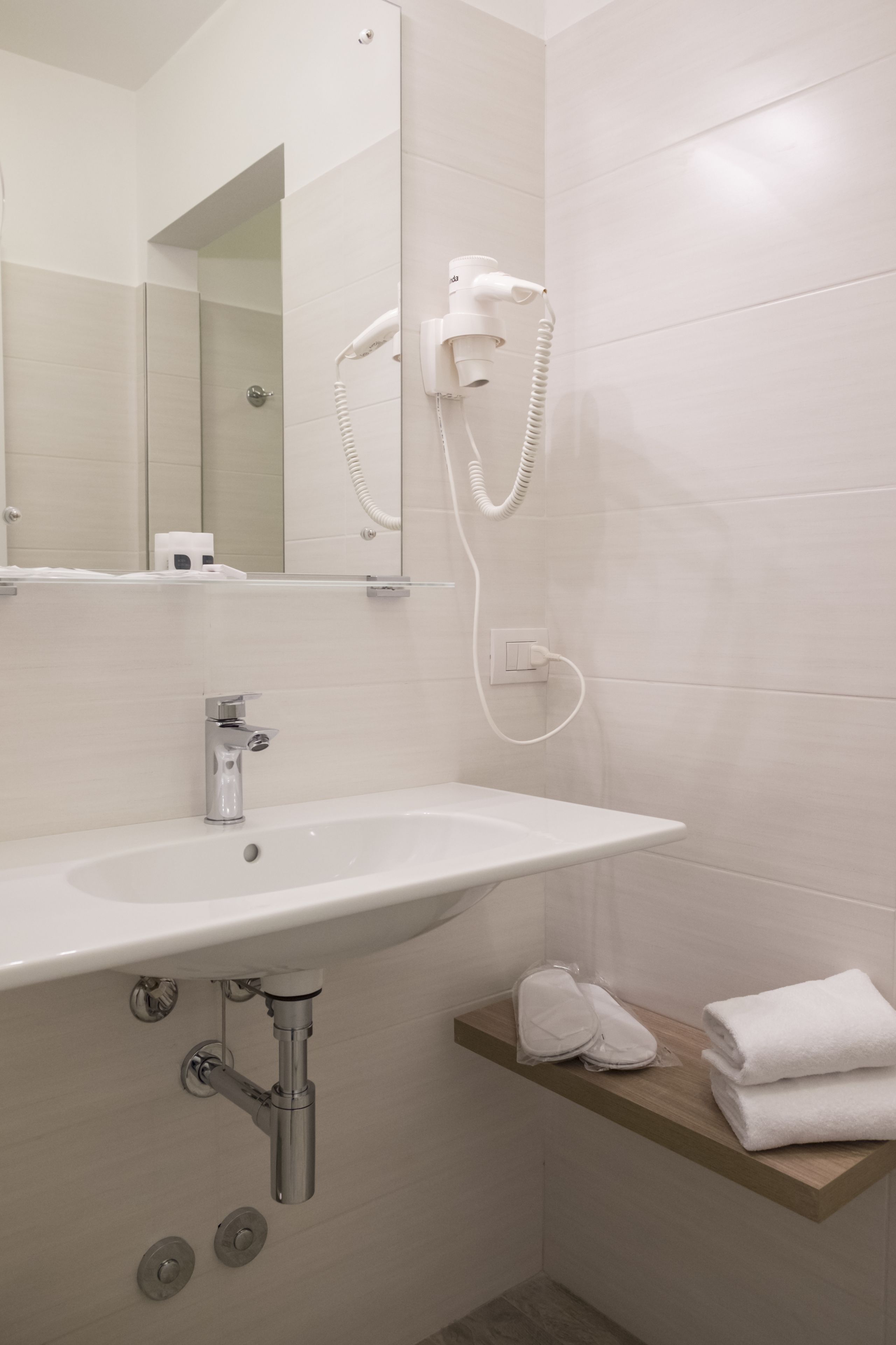 Ein Badezimmer mit einem weißen Waschbecken, einem Spiegel und einem an der Wand befestigten Föhn.