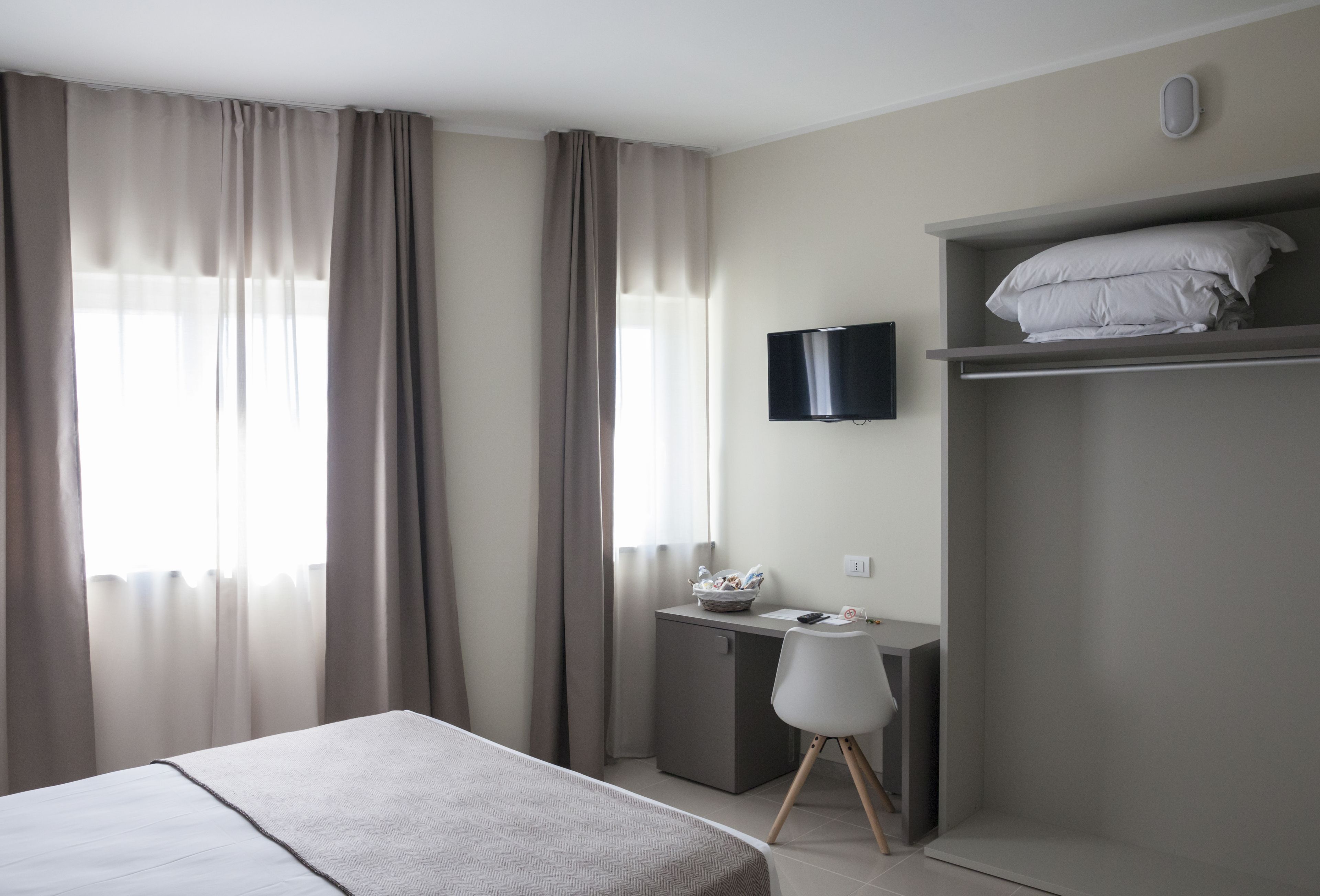 A modern hotel room with a bed, a desk, a chair, a TV, and a wardrobe.