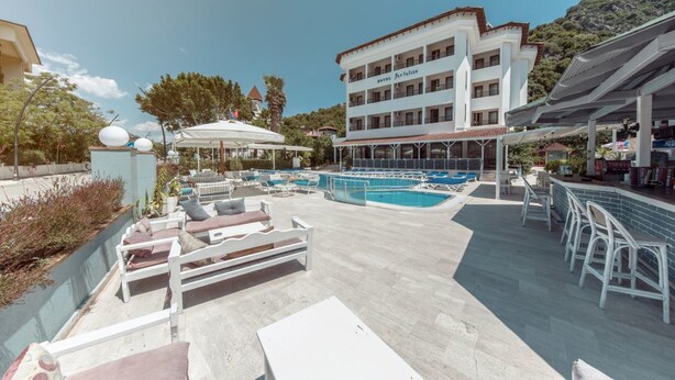 A pool area with lounge chairs and umbrellas, a building with balconies, and a mountainous backdrop. - Portofino Hotel (Marmaris)