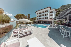 A pool area with lounge chairs and umbrellas, a building with balconies, and a mountainous backdrop. - Portofino Hotel (Marmaris)