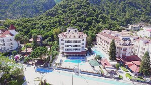 A hotel with a swimming pool, surrounded by lush greenery and multiple buildings. - Portofino Hotel (Marmaris)