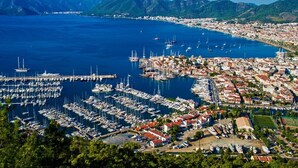 A marina with numerous boats docked, surrounded by a coastal town with buildings and mountains in the background. - Portofino Hotel (Marmaris)