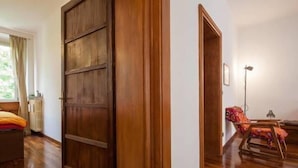A room with a wooden door, a bed with a colorful blanket, a chair, and a floor lamp. - Veronetta Apartment (Verona)