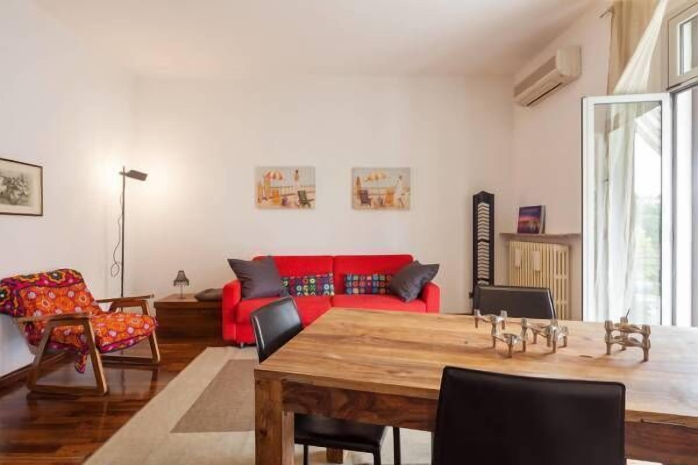 Een moderne woonkamer met een houten eettafel, een rode bank en een kleurrijke fauteuil.
