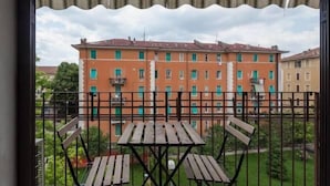 A balcony with a wooden table and chairs, overlooking a row of buildings with green windows. - Veronetta Apartment (Verona)