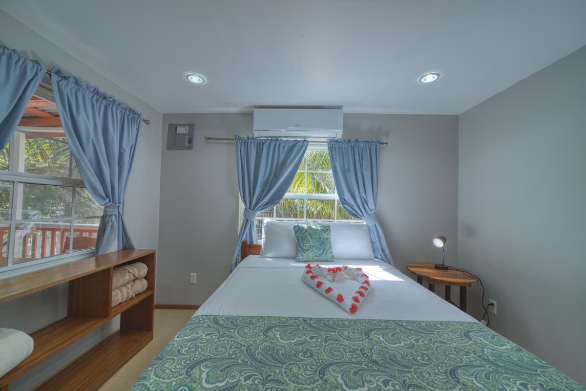 A bedroom with a bed, a bedside table with a lamp, a window with curtains, and a built-in shelf.