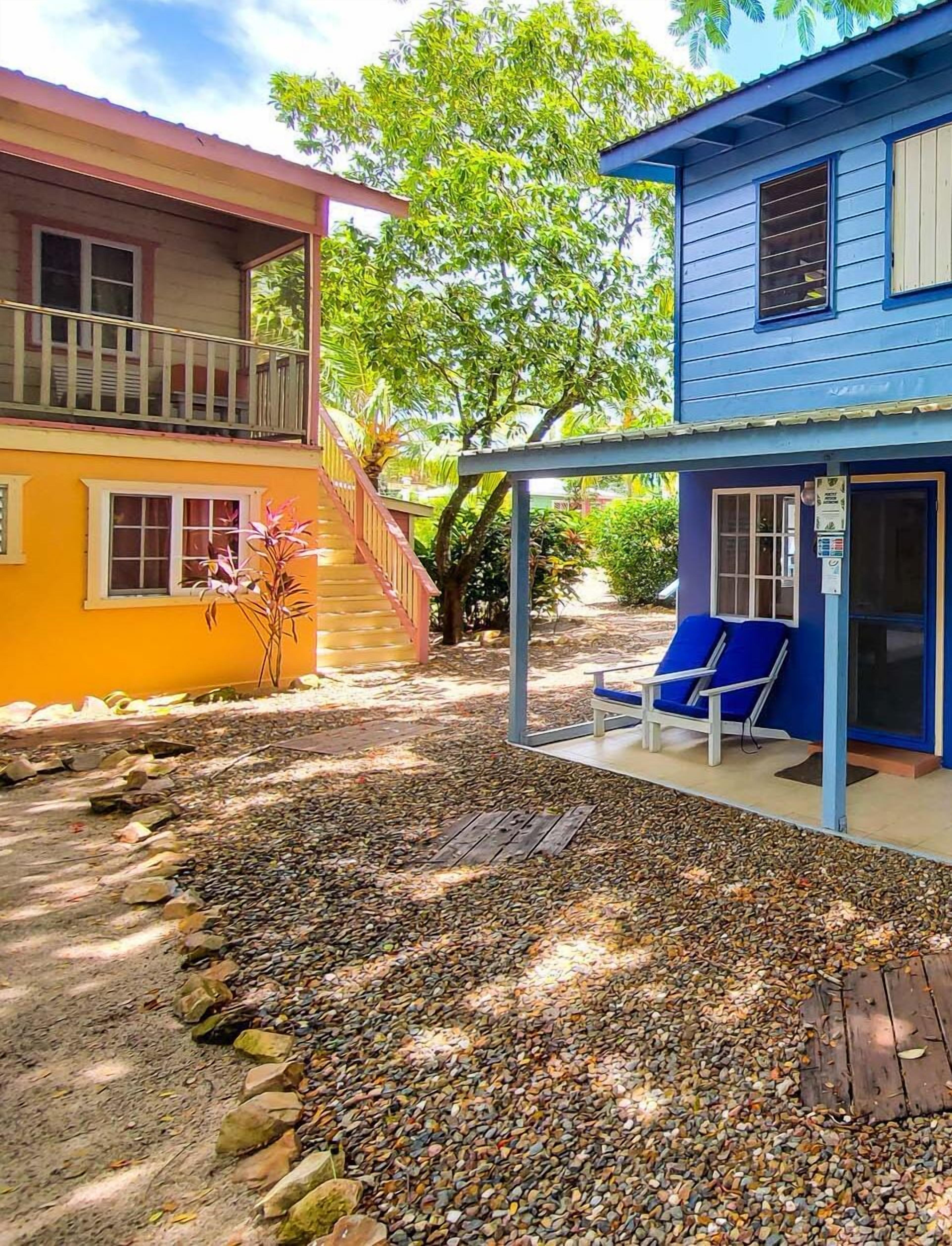 Un bâtiment à deux étages doté d’un patio couvert, d’une terrasse en bois et d’un petit jardin agrémenté de galets et de plantes.
