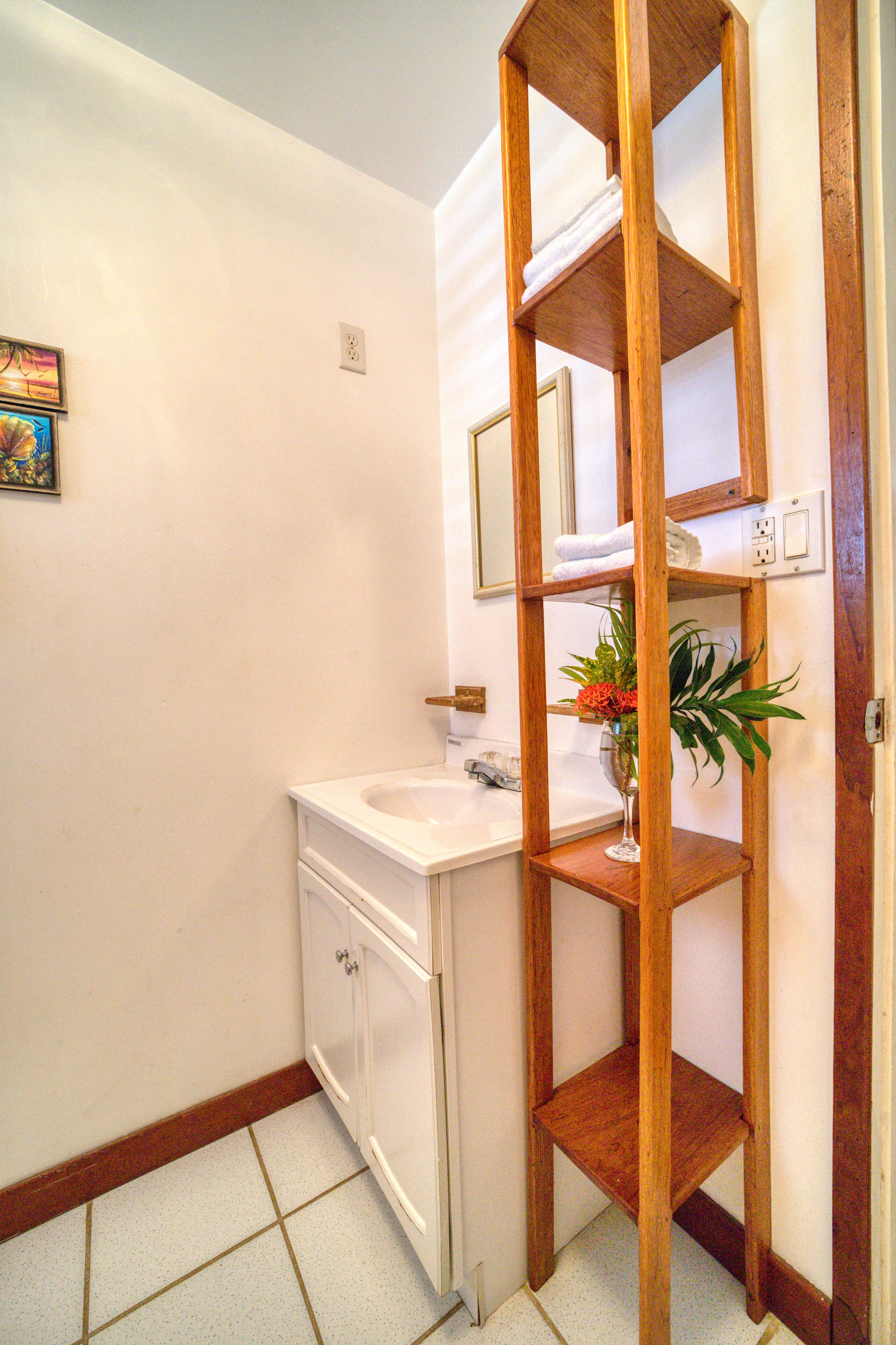 A bathroom with a wooden shelf, a white sink, and a mirror above it.