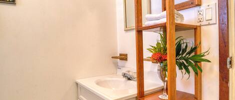 A bathroom with a wooden shelf, a white sink, and a mirror above it.