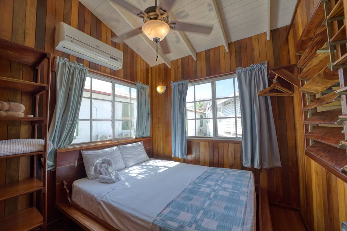 A wooden cabin bedroom with a bed, a ceiling fan, and a window with curtains.