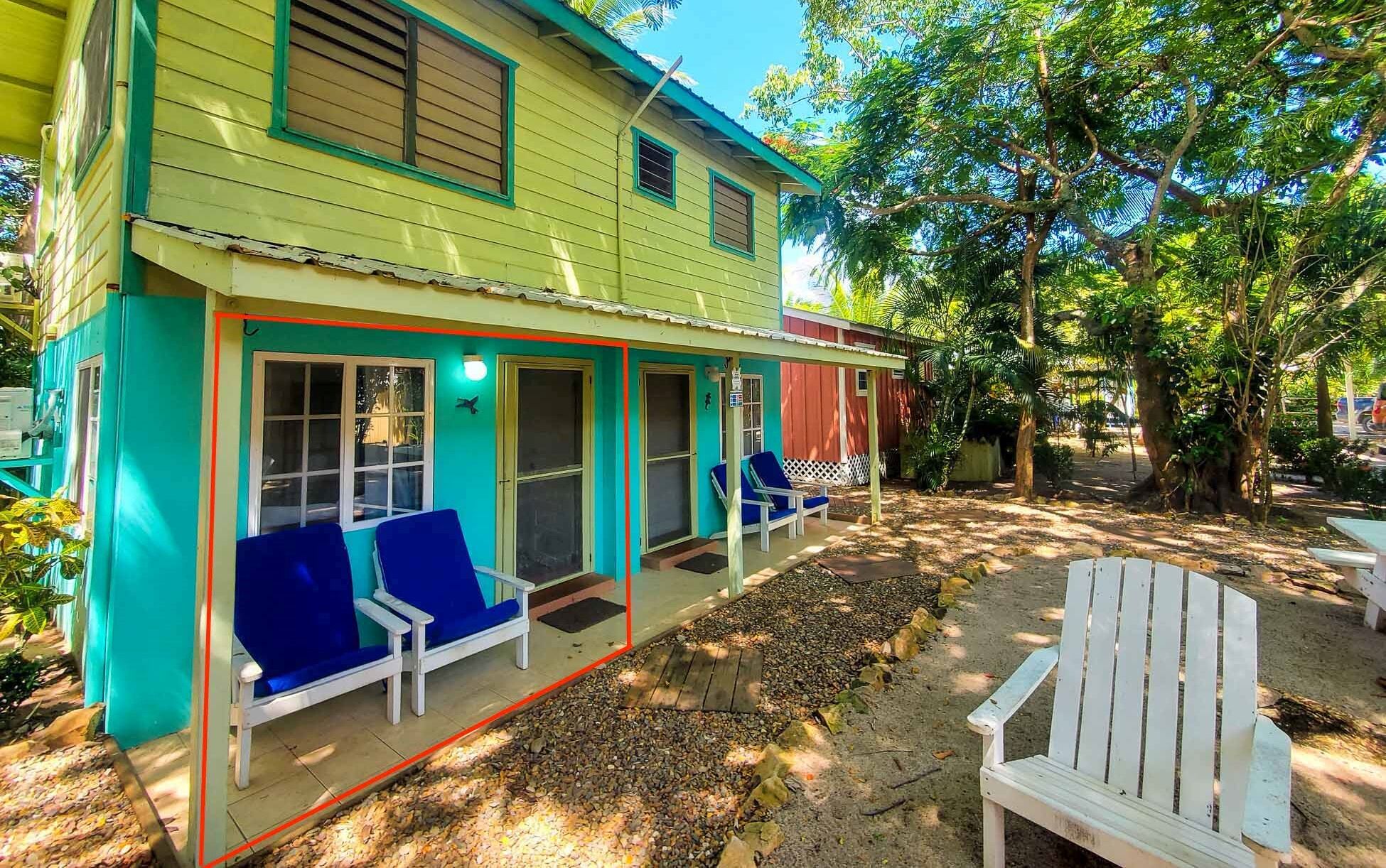 Ein zweistöckiges Haus mit einer Veranda, zwei blauen Stühlen und einem weißen Stuhl draußen.