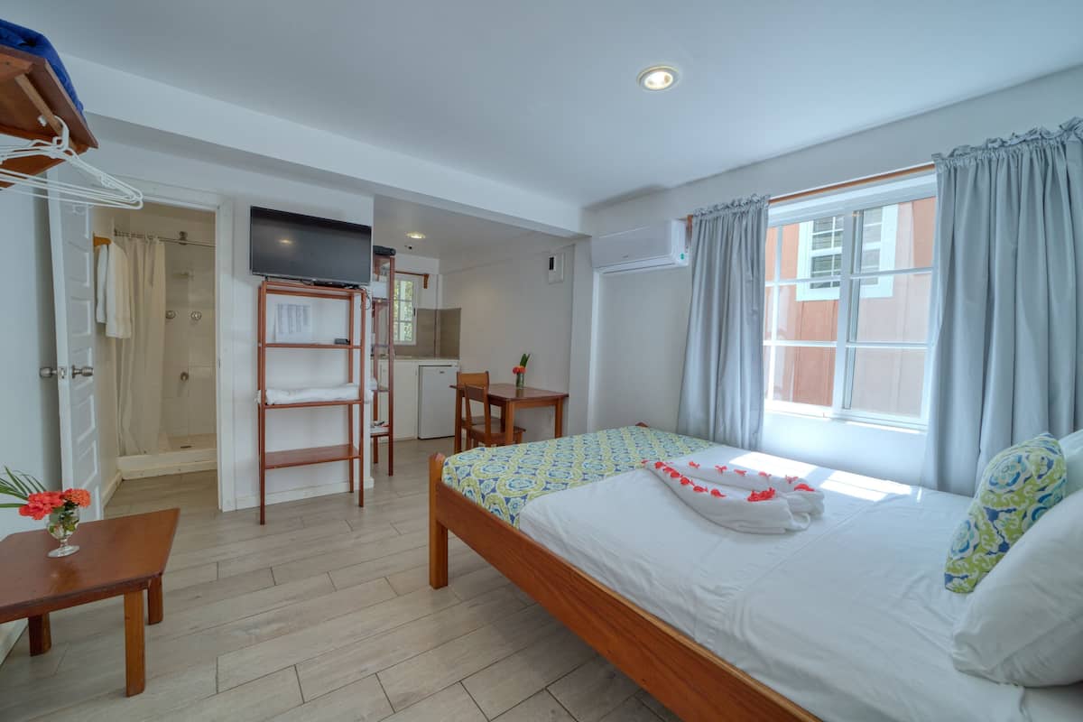 A hotel room with a bed, a desk, a chair, a small table with a vase of flowers, and a shower area.
