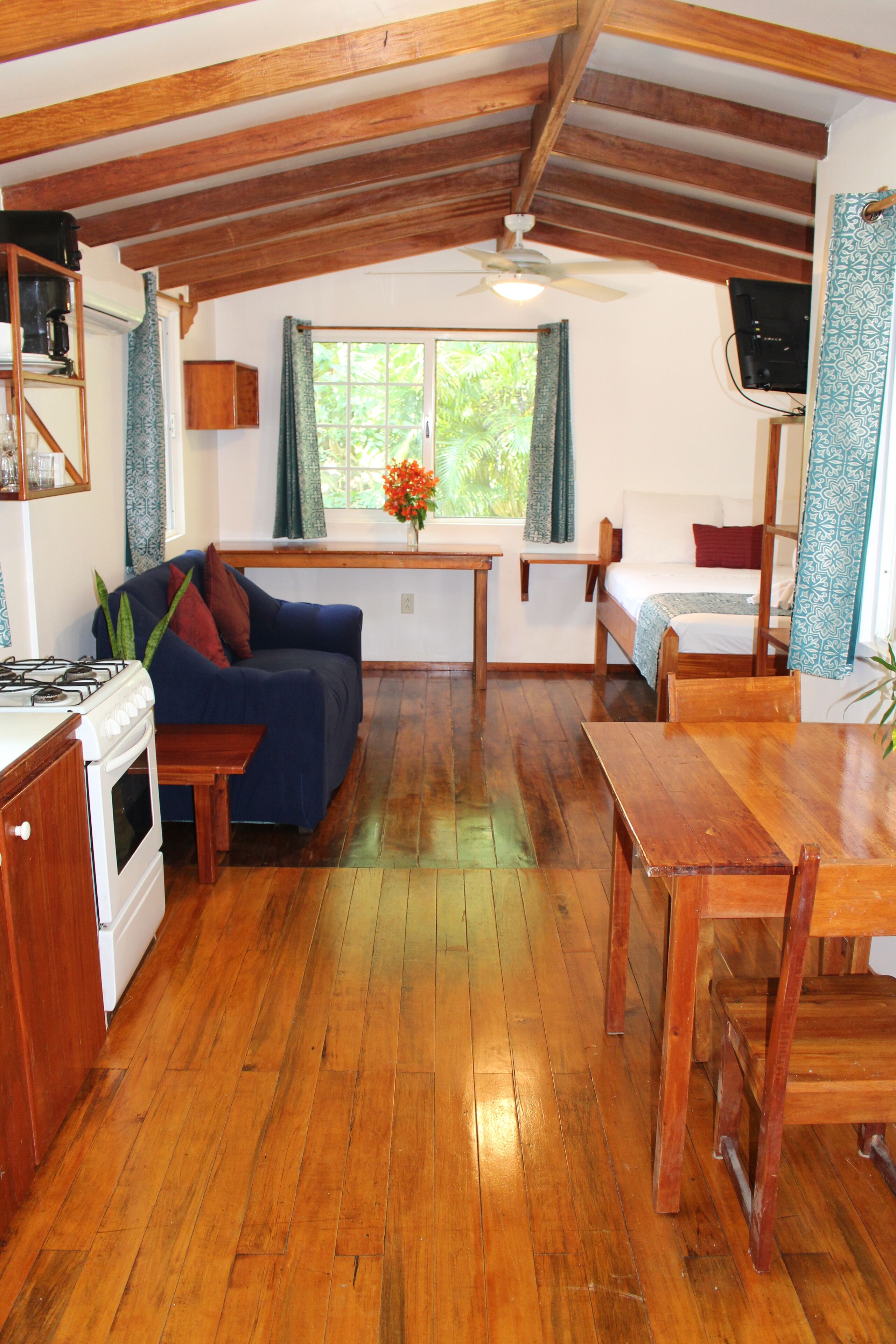 A cozy kitchen with wooden beams, a dining table, a sofa, and a bed with a window view.