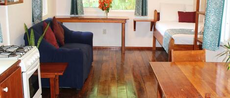 A cozy kitchen with wooden beams, a dining table, a sofa, and a bed with a window view.