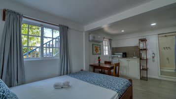 Een slaapkamer met een bed, een raam met gordijnen, een eettafel en een kitchenette.