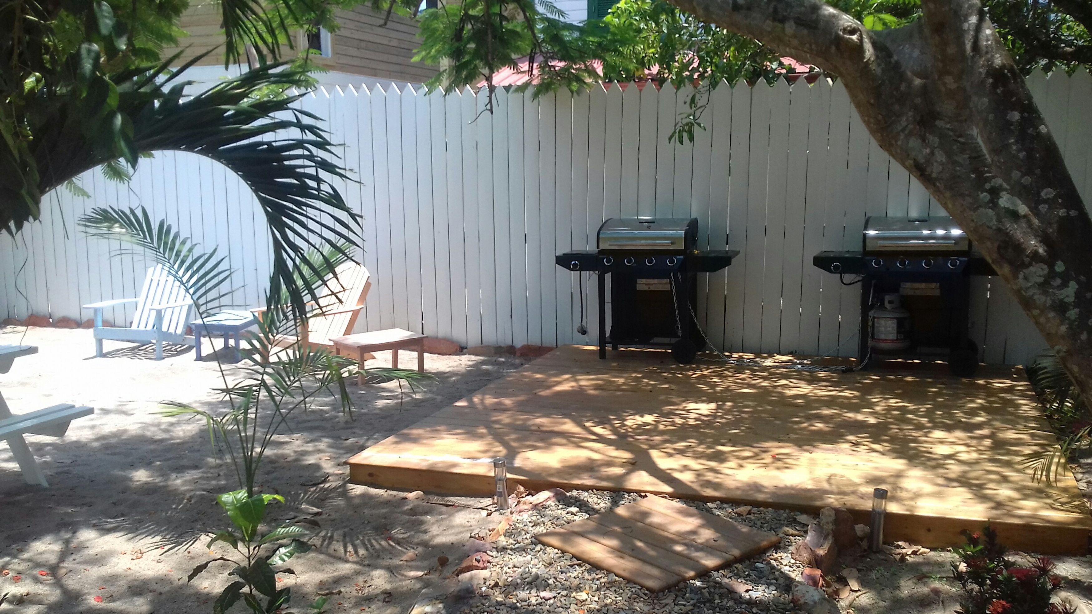 Un jardin avec deux barbecues, une terrasse en bois et une clôture blanche.