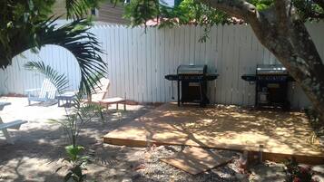 Un jardin avec deux barbecues, une terrasse en bois et une clôture blanche.