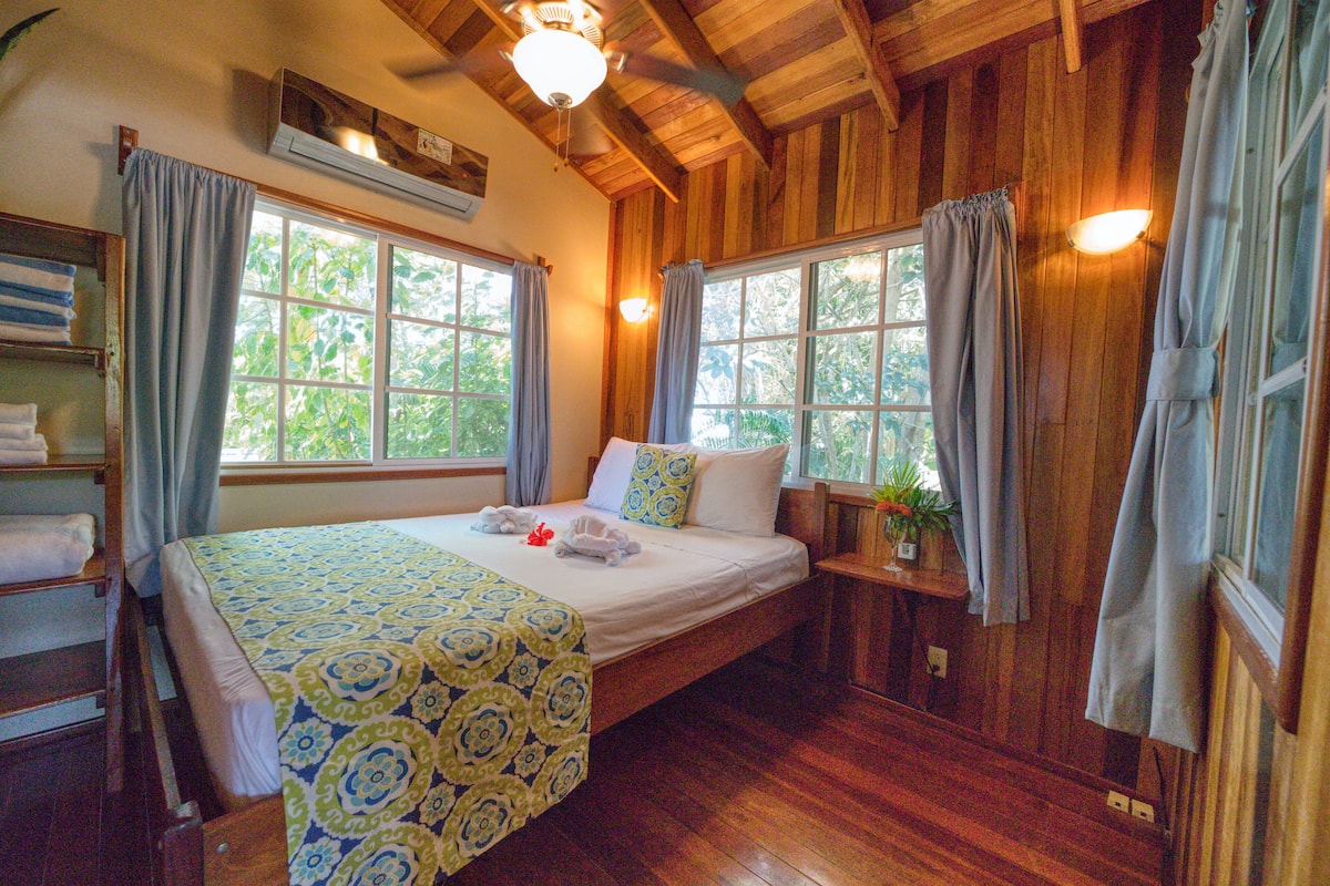A wooden-paneled room with a bed, a shelf with towels, and a window with curtains.