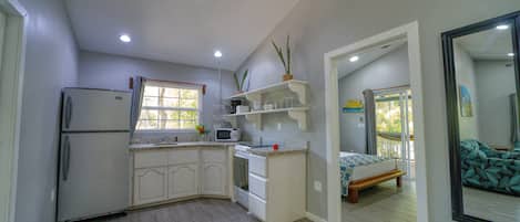 A compact kitchen with a refrigerator, microwave, and stove, leading to a bedroom with a bed and a balcony.